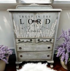 an old dresser with the words trust in the lord painted on it next to some lavender flowers