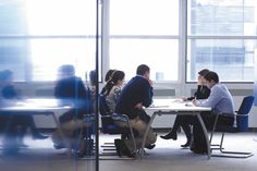 a group of people sitting at a table in an office setting with one person talking to the other