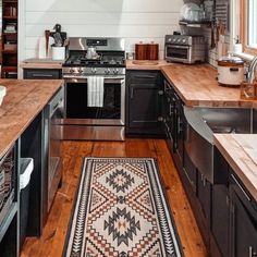 a kitchen with wood floors and black cabinets, an oven, sink, stove top and microwave