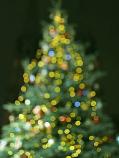 a lit christmas tree in front of a window with blurry lights on the branches