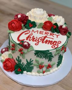 a merry christmas cake with red and white frosting roses on the top is sitting on a plate