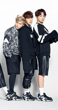 three young men standing next to each other in front of a white wall wearing black and white clothing