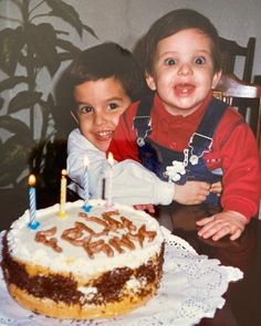 two young children sitting in front of a birthday cake