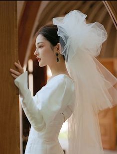 a woman in a white wedding dress is holding her veil over her head and looking off to the side