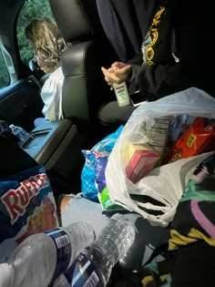 a man sitting in the back seat of a car filled with plastic bags and bottles