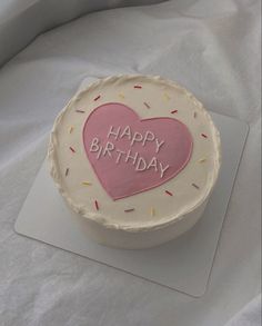 a birthday cake that is on top of a white table cloth with pink frosting and sprinkles