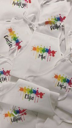 many white aprons with different colors and designs on them, all have names painted on them