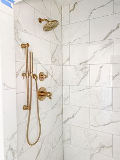 the shower head is gold in color and it's marbled walls are white