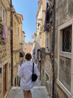 a woman walking down an alley way with clothes hanging out to dry