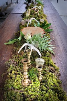 an arrangement of plants and candles on a long wooden table with moss growing all over it