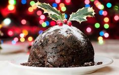 a christmas pudding on a plate with holly berry decoration and colorful lights in the background