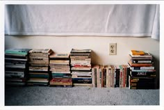 several stacks of books sitting on the floor in front of a white wall and window