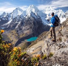 a man with a backpack standing on top of a mountain looking at the snow covered mountains