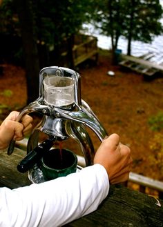 a person is filling a cup with water from a faucet on a picnic table