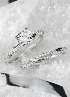 two wedding rings sitting on top of snow with diamonds in the middle and one diamond between them