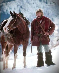 a man standing next to a horse in the snow