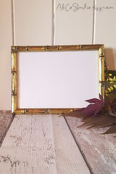 an empty gold frame sitting on top of a wooden table next to a potted plant