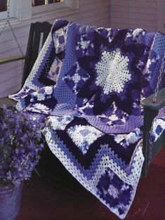 a purple and white crocheted blanket sitting on a porch swing next to a potted plant