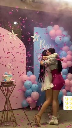 two women hugging each other in front of balloons and confetti on the wall