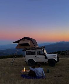 two people sitting on the ground in front of a vehicle with a tent over it