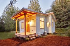 a small white house sitting on top of a dirt field next to trees and grass