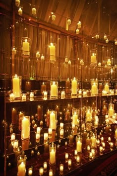 rows of lit candles are lined up against a wall in a room with glass walls