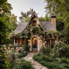 a small house with lots of flowers on the front and side of it, surrounded by greenery