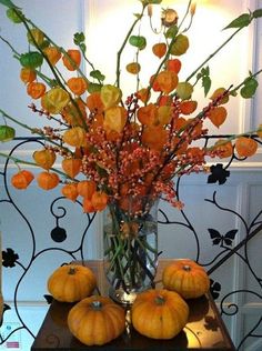 an arrangement of pumpkins and flowers in a vase on top of a wooden table