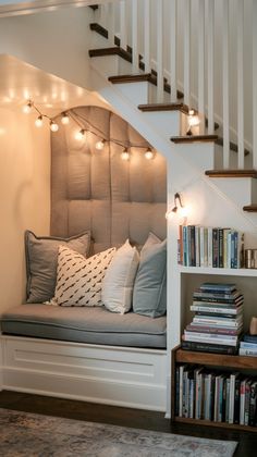 there is a bench under the stairs with books on it and some lights hanging above