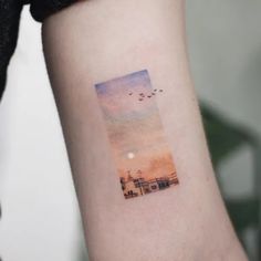 a small watercolor painting on the arm of a woman with birds flying over her head