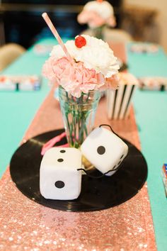 two dices on a black plate with pink flowers in a vase and other decorations