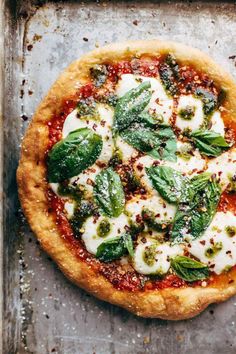 a pizza sitting on top of a metal pan covered in cheese and green leafy toppings