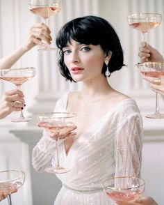 a woman in a white dress holding up wine glasses with pink liquid and champagne being poured into them