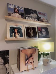 some books are sitting on a shelf above a table with a cup and lamp in front of them