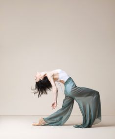 a woman in a white shirt and green pants is doing a handstand on the floor