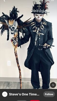 a man dressed up as a skeleton holding a stick and wearing a hat with feathers on it