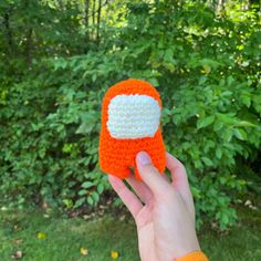 a hand holding an orange and white crocheted object in front of some bushes