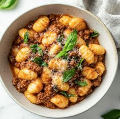 a bowl filled with pasta and sauce on top of a white table cloth next to a spoon