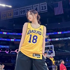 a female basketball player in a yellow jersey and black shorts stands on the court with her hands behind her back