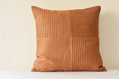 a brown pillow sitting on top of a bed next to a white wall and wooden headboard