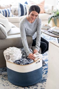 a woman sitting on the floor next to a blue and white basket filled with clothes