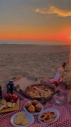 a picnic table on the beach at sunset with pizza, cookies and drinks in front of it