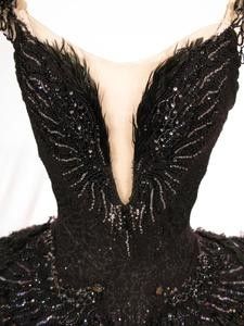 the back of a black dress with sequins and feathers on it's shoulders