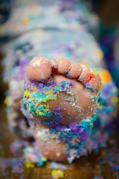 a baby's foot covered in colorful powder on top of a wooden table with sprinkles