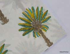 an embroidered palm tree on white fabric with blue and yellow accents is featured in this image