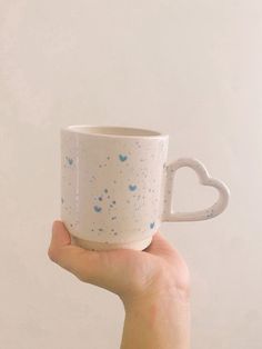 a hand holding a white coffee cup with blue speckles