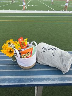 a basket with candy and sunflowers sits on a bench in front of a football field