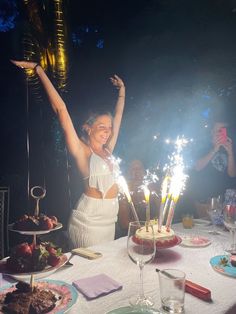 a woman is celebrating her birthday with sparklers in front of her and cake on the table