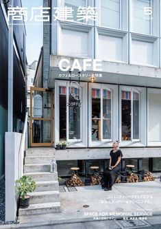 a person sitting on a bench in front of a building with windows and stairs leading up to it