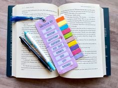 an open book with colorful sticky notes and pens on it next to a fountain pen